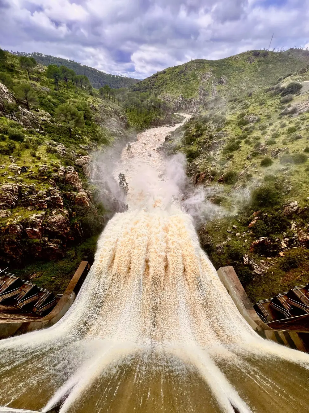 Aliviadero de la presa de Olivargas soltando agua hacia el río, entre laderas de monte